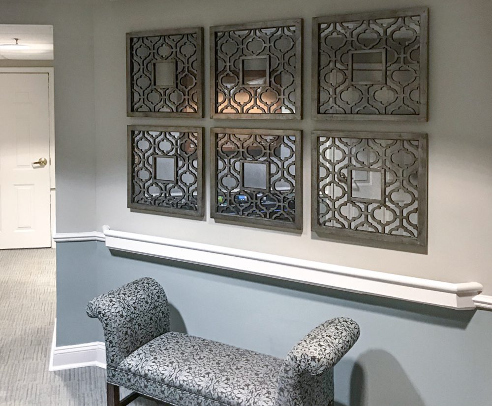 arrangement of decorative mirrors above floral bench in senior living hallway